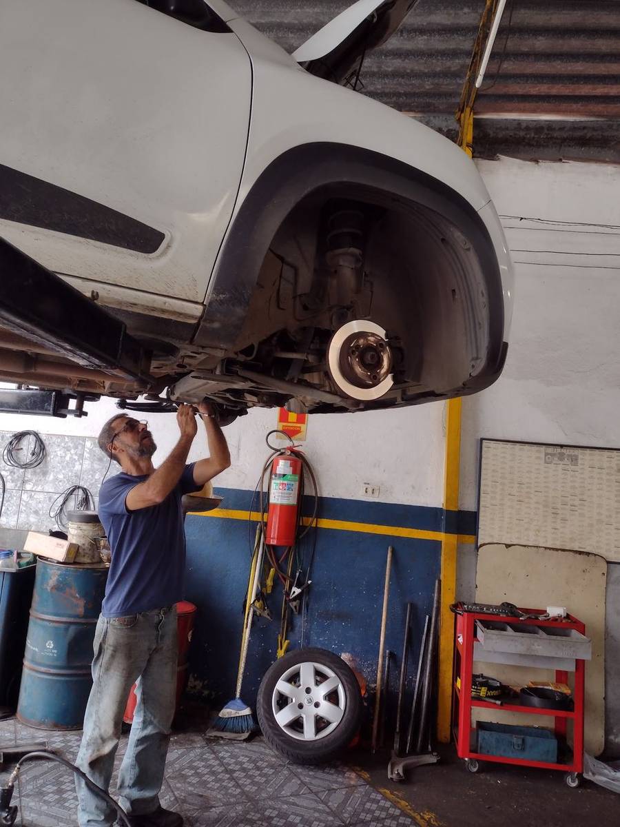 Mecânico da Munhoz revisando o disco de freio e a suspensão dianteira de um carro elevado